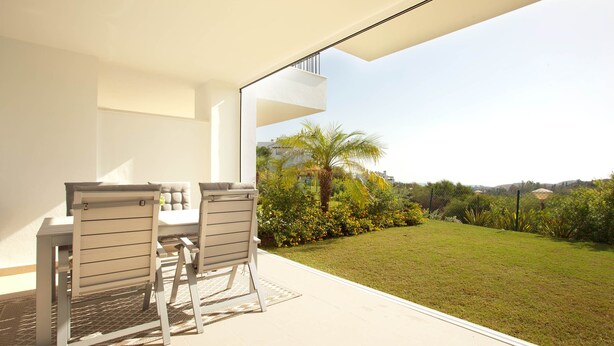 Une terrasse extérieure moderne, avec une table et des chaises, donnant sur une pelouse bien entretenue et un bâtiment situé au loin.
