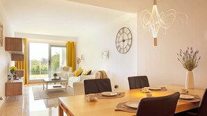 Un espace de salle à manger moderne avec une table en bois dressée pour quatre personnes, une grande horloge murale et un luminaire décoratif.