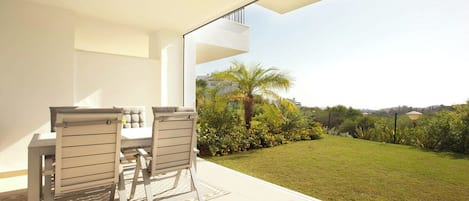 An outdoor patio area with a table and chairs, a view of a well-maintained lawn, and a clear sky.