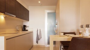 Une cuisine moderne avec un coin repas, dotée d’un plan de travail blanc, de meubles de rangement sombres et d’une porte en verre donnant sur une autre pièce.