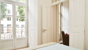 Een slaapkamer met een bed, een stoel en een deur naar een balkon.