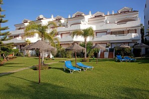 Un hotel con varios balcones, un césped cuidado y numerosas sillas de descanso.