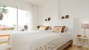 A bedroom with a large bed, a bedside table with a lamp, and a view of the outdoors.