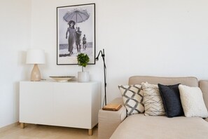 Un dormitorio con una cama, una mesita de noche con lámpara, un cuadro en la pared y una planta pequeña.