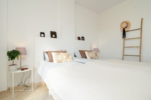 Un dormitorio con una cama grande, mesitas de noche, una lámpara, una planta y una escalera apoyada en la pared.