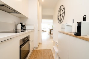 Una cocina moderna con armarios blancos, horno empotrado, cafetera y panera.