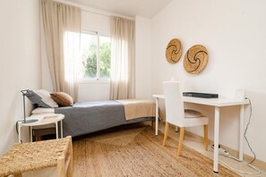Un dormitorio compacto con cama, mesita de noche, silla, escritorio y ventana con cortinas.