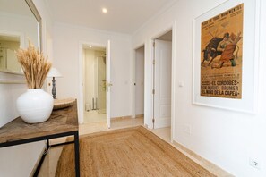 A hallway with a white door, a framed poster, and a vase on a table.