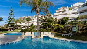 A swimming pool with a clear blue water feature, surrounded by lush greenery and white buildings with balconies.