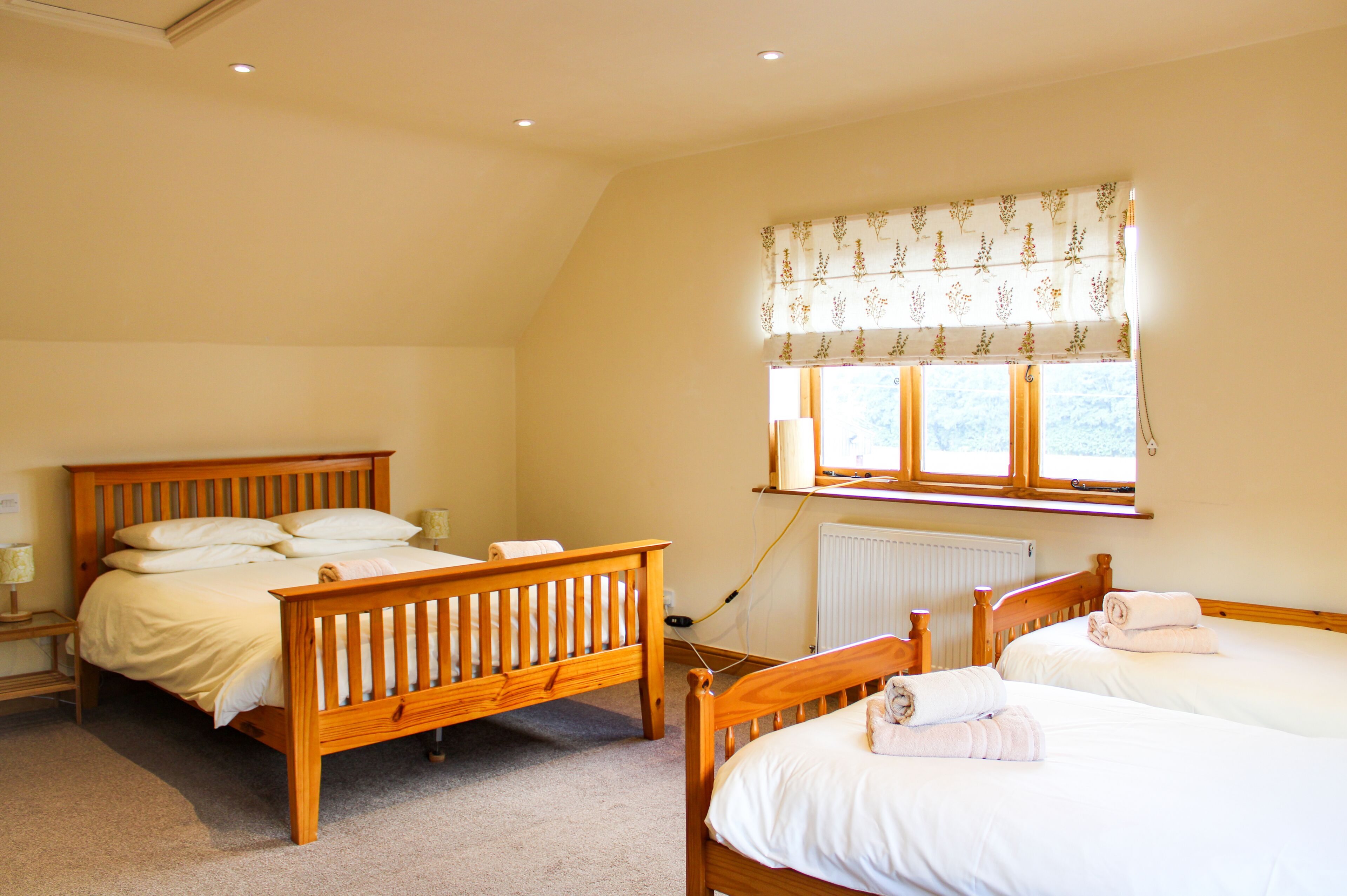 Une chambre avec deux lits en bois, une fenêtre ornée de rideaux à motifs floraux et un radiateur.