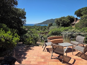 A patio with outdoor furniture, a view of the sea, and surrounding greenery.