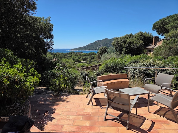 A patio with outdoor furniture, a view of the sea, and surrounding greenery.