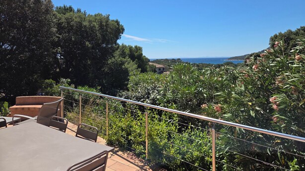 En terrasse med et bord og stole, der giver udsigt over et kystlandskab med træer og havudsigt.