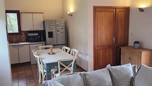 En hyggelig stue med sofa, spisebord med stole, et køkkenområde med køleskab og mikroovn samt træbjælker i loftet.