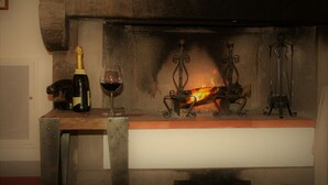 A fireplace with a fire, a bottle of wine, and a glass on a wooden shelf. - Podere I Rovai-apt IL RIFUGIO-amazing view Tuscany (Reggello ( Firenze ))