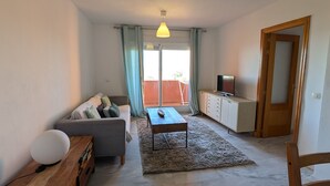 A compact living space with a sofa, a coffee table, a wooden cabinet, a TV, and a door leading to an outdoor area. - 201 Apartamento La Duna (Tarifa)