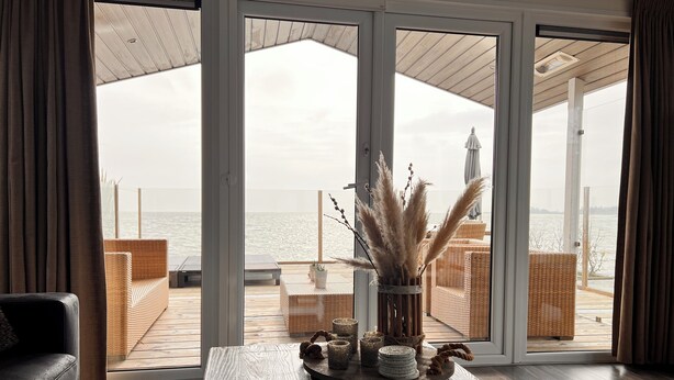 Ett modernt vardagsrum med en stor skjutdörr i glas som leder ut till en balkong med utsikt över havet.