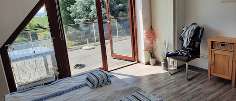 Quarto com uma grande porta de vidro deslizante que dá para uma varanda, uma cama com roupa de cama listrada, um armário de madeira e uma cadeira.