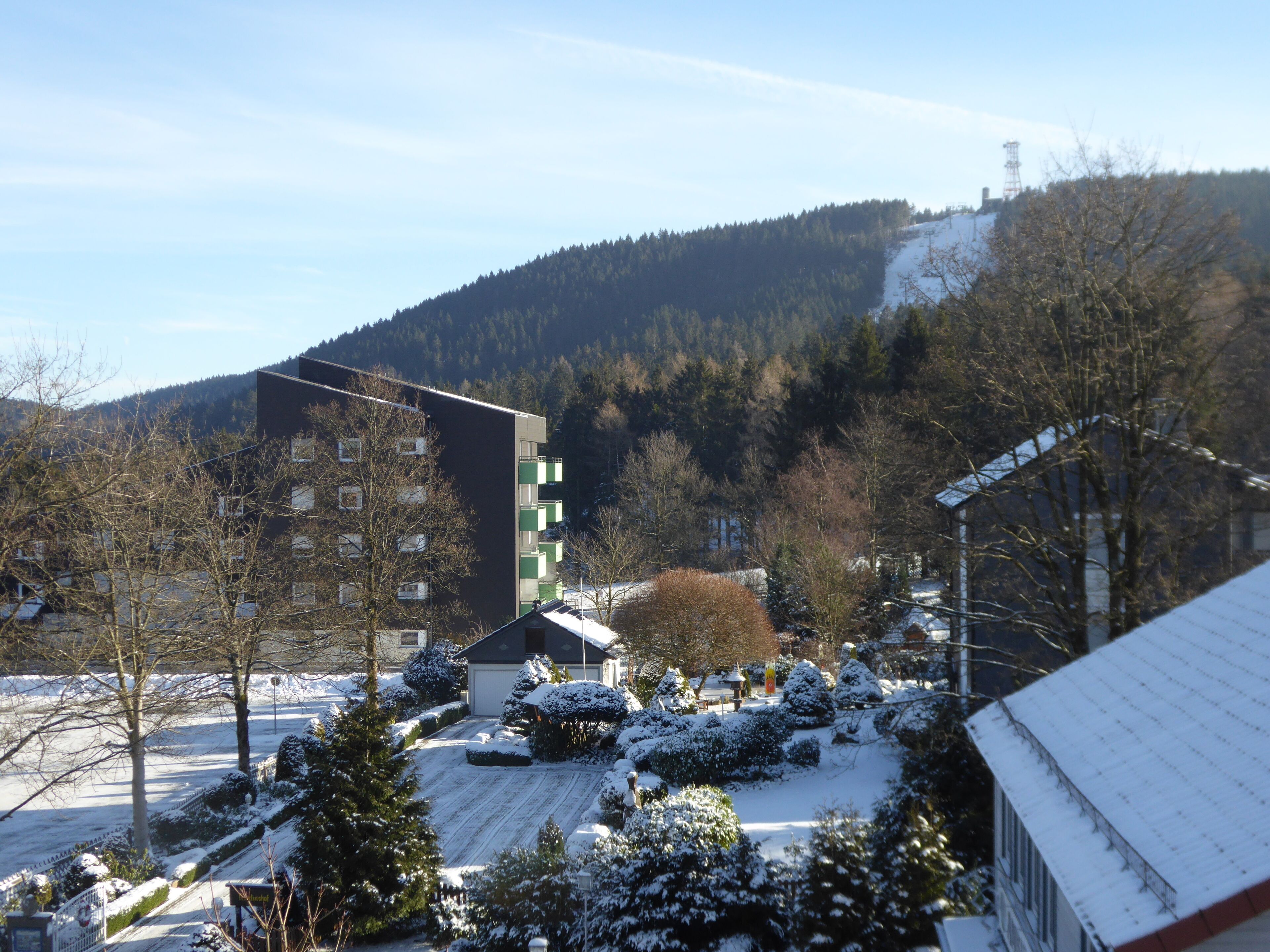 A residential area with a modern building, snow-covered trees, and a hilly backdrop.