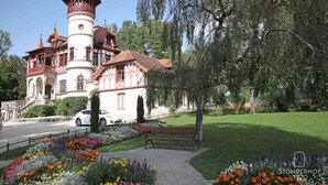 Ein historisches Gebäude mit einem Turm, umgeben von einem gepflegten Garten und einer Bank.