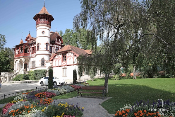 A historic building with a tower, surrounded by a well-maintained garden and a bench.
