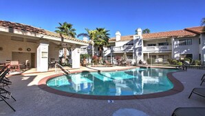 A pool area with a clear blue pool, lounge chairs, and a covered seating area.