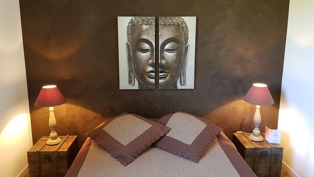 Een slaapkamer met een bed, twee nachtkastjes, twee lampen en een kunstwerk aan de muur.