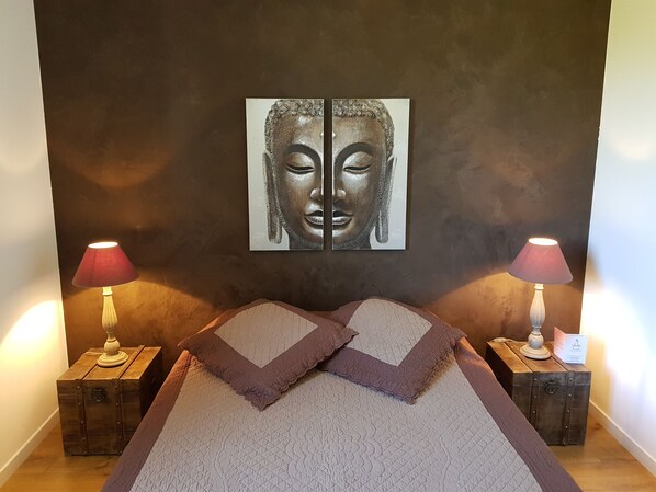 A bedroom with a bed, two nightstands, two lamps, and a wall-mounted artwork.