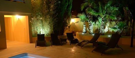 Un espace piscine comprenant des chaises longues, un jacuzzi et une terrasse bien éclairée.