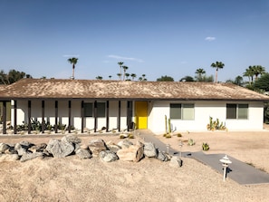 A single-story building with a flat roof, a yellow door, and a row of windows with shutters. - Just listed - The Enticing Villa Cardona, Magnesia Falls, Rancho Mirage (Rancho Mirage)