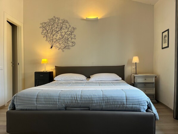 A neatly made bed with striped bedding, two bedside tables with lamps, a wall-mounted light fixture, and a framed picture on the wall.