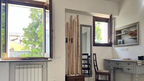 Une pièce avec un radiateur, une chaise en bois, un bureau avec des tiroirs, un miroir et une fenêtre avec des stores.