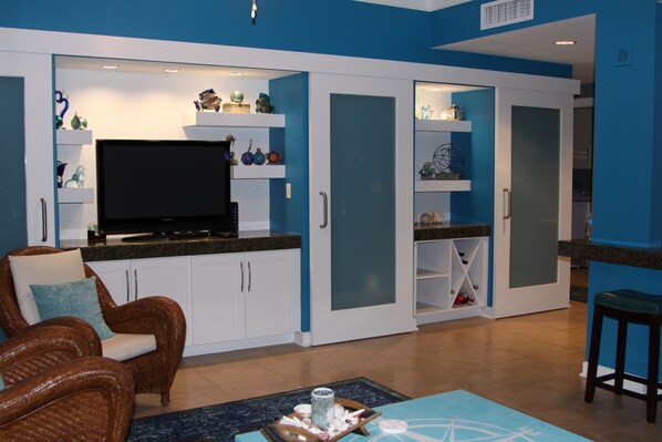 Una sala de estar moderna con televisor de pantalla plana, mobiliario de mimbre y objetos decorativos en estantes.