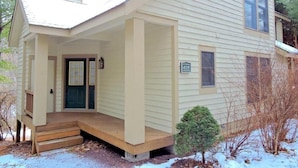 A two-story house with a covered porch, a front door, and a small front yard with a tree.