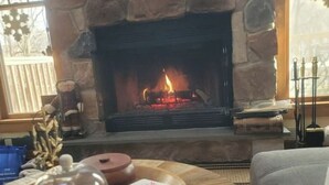 A cozy living room with a stone fireplace, a round wooden coffee table with a glass of wine, and a comfortable couch.