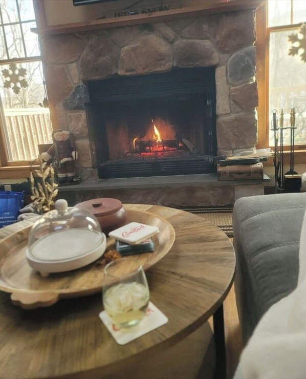 A cozy living room with a stone fireplace, a round wooden coffee table with a glass of wine, and a comfortable couch.