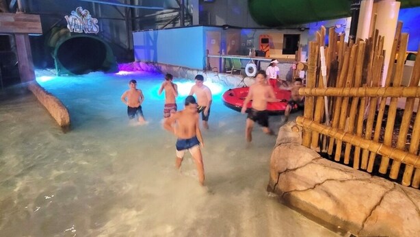 A water park with a large indoor pool, slides, and a wooden play structure.