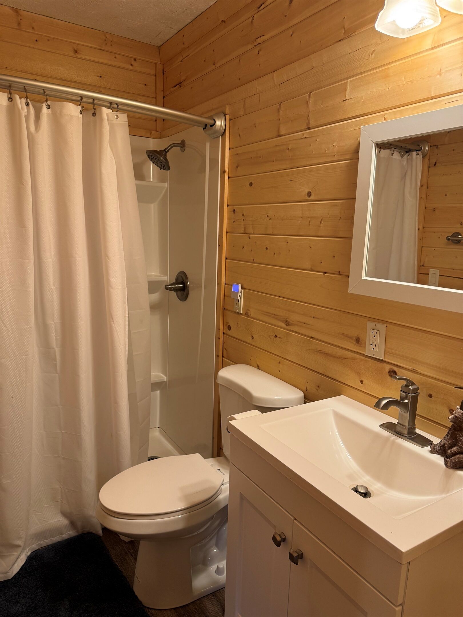 Une salle de bain aux murs lambrissés, équipée de toilettes, d’un lavabo et d’une douche.