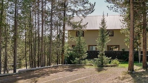 A two-story building with a metal roof, surrounded by tall pine trees.