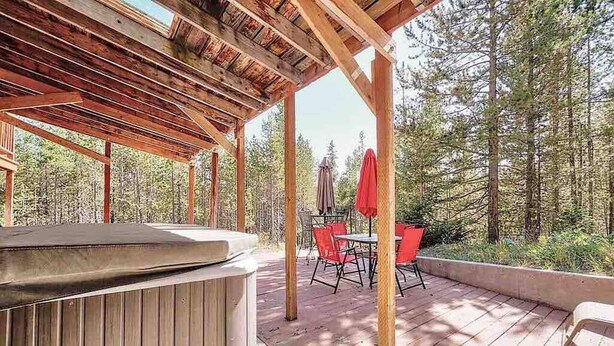 An outdoor deck with a hot tub, red chairs, and a table.