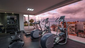 Un gimnasio con cintas de correr y pesas, amplias ventanas con vistas a la ciudad y un diseño interior moderno.