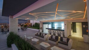 Un espacio de descanso al aire libre con mobiliario moderno, un bar y vistas a la ciudad.