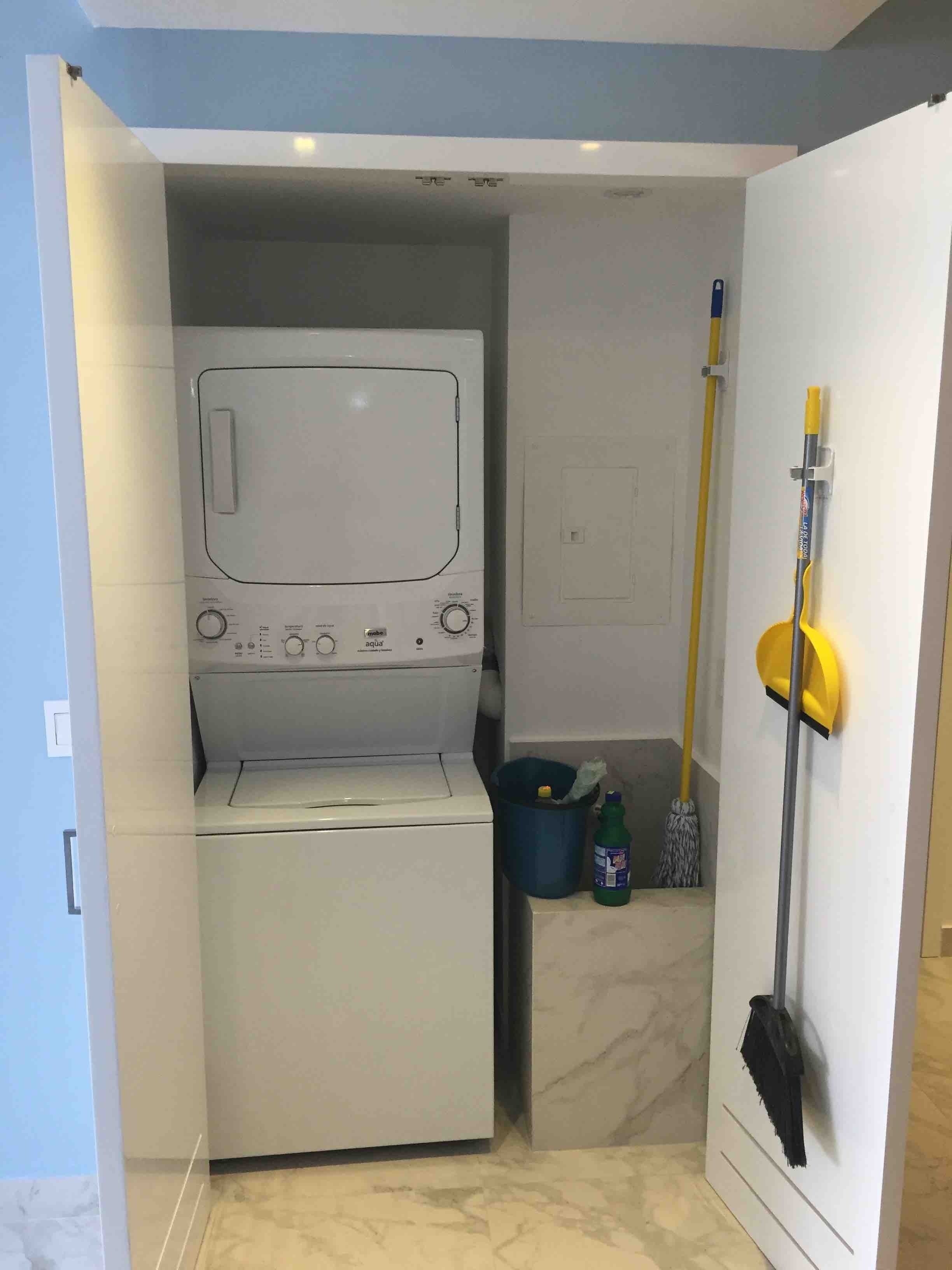 A compact laundry room with a washing machine and dryer, a mop, and cleaning supplies.