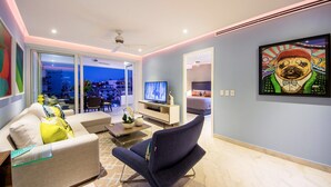 Una sala de estar moderna con un sofá, un sillón oscuro, un televisor y un cuadro en la pared.