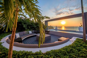 Un espace de détente extérieur moderne, doté d’un aménagement de sièges incurvé, d’une piscine et d’une vue sur le coucher de soleil sur l’eau.