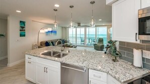 A modern kitchen with granite countertops, stainless steel appliances, and pendant lighting. - Crystal Sands Tower Unit 903 - Beachfront (Sarasota)