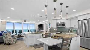 A modern kitchen with white cabinets, stainless steel appliances, and pendant lighting. - Crystal Sands Tower Unit 903 - Beachfront (Sarasota)