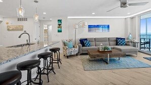 A modern living room with a grey sofa, a wooden coffee table, and a bar area with stools. - Crystal Sands Tower Unit 903 - Beachfront (Sarasota)