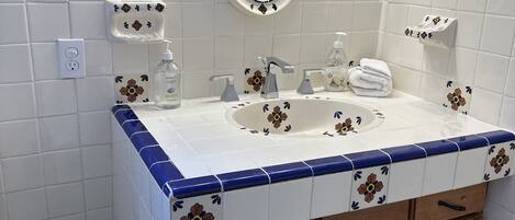 Et badeværelse med en hvid vask, blå flisearbejdsbordplade, træskabe, et spejl og en toiletpapirholder.