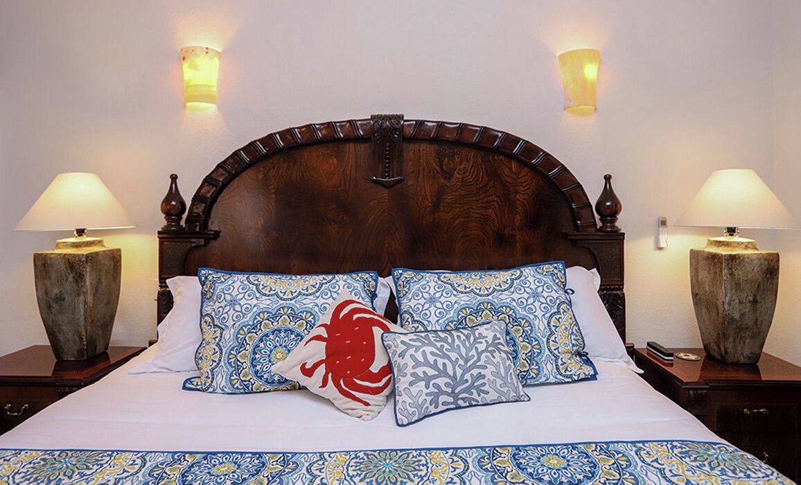 A neatly made bed with patterned pillows and a matching bedspread, flanked by two nightstands with lamps and decorative vases.